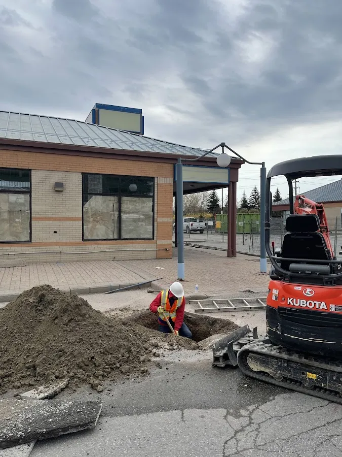Heavy equipment excavator performing sewer line replacement in front of commercial building