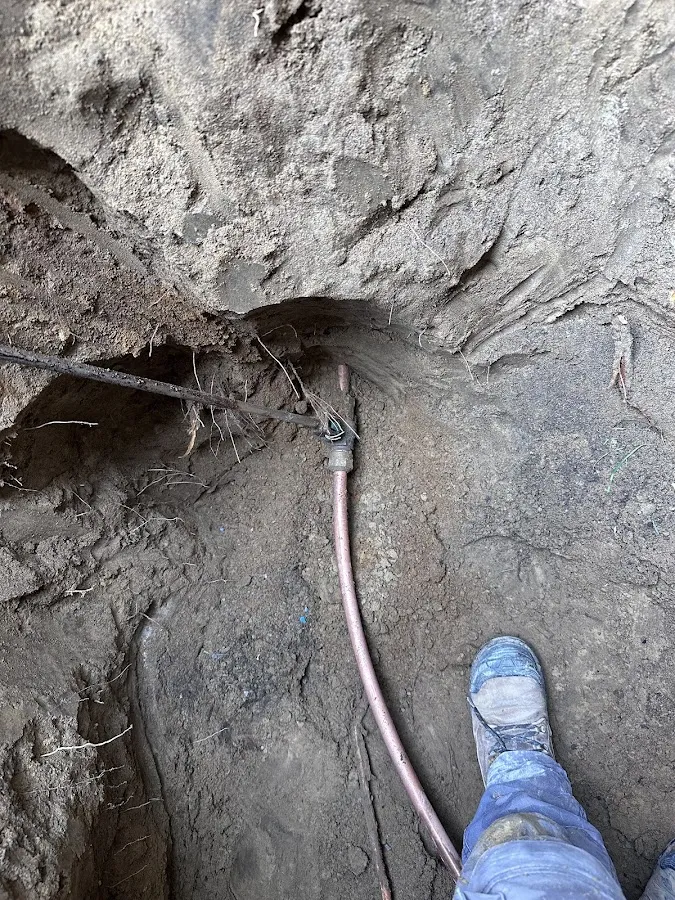 Close-up of excavated underground piping with worker marking damage location